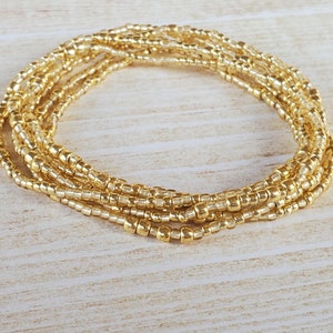 May include: A gold beaded waist chain, also known as a waist bead or belly chain, is made of small, round beads strung together in a continuous loop. The chain is designed to be worn around the waist, and it can be adjusted to fit different sizes.