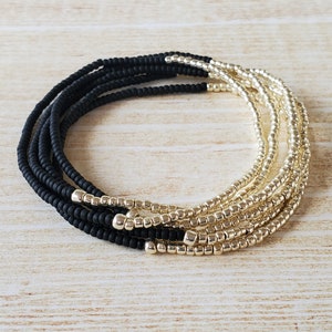 May include: A black and gold beaded bracelet with multiple strands. The bracelet is made of small, round beads and has a two-tone design.