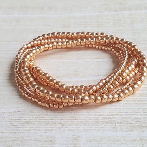 May include: A set of four gold-toned beaded bracelets, layered and intertwined, creating a delicate and elegant look.
