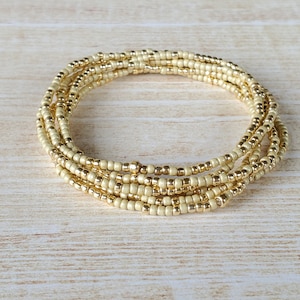 May include: A multi-strand beaded bracelet made of cream-colored beads with gold accents.