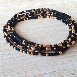 May include: A multi-strand beaded bracelet with black and rose gold beads. The bracelet is made of small, round beads and is wrapped around itself multiple times.