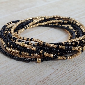 May include: A black and gold beaded waist chain with multiple strands of beads. The chain is made of small, round beads and has a simple, elegant design.