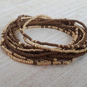 May include: A multi-strand beaded bracelet with brown and gold beads. The bracelet is made of many thin strands of beads that are woven together.