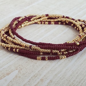 May include: A multi-strand beaded bracelet with alternating burgundy and gold beads.