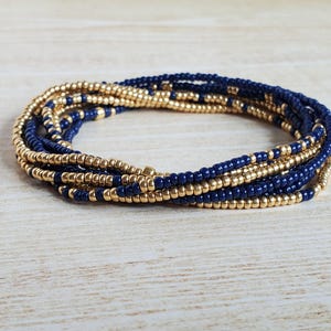 May include: A multi-strand beaded bracelet with alternating gold and dark blue beads.