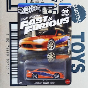 Op de afbeelding: Een Hot Wheels Silver Series speelgoedauto in een blisterverpakking. De oranje en blauwe Nissan Silvia (S15) maakt deel uit van de Fast & Furious Graphic Remix-serie. De verpakking bevat de logo's van Hot Wheels en Mattel.