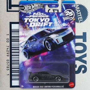 Puede incluir: Un coche de juguete Hot Wheels Silver Series, un modelo a escala de un Nissan 350Z negro con detalles plateados, de la serie Fast & Furious: Tokyo Drift. El embalaje presenta un gráfico de paisaje urbano y el texto "TOKYO DRIFT".