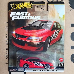 May include: A Hot Wheels Premium die-cast car from the Fast & Furious series. The red Lancer Evolution IX model features black and white graphics and the text "RAYS". The packaging includes the Hot Wheels logo and the text "2/5".