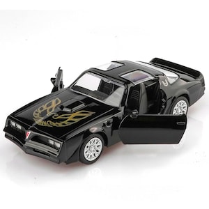May include: Black die-cast model car with open doors. The car features a gold emblem on the hood and silver wheels. The car has a sunroof and is a classic muscle car.