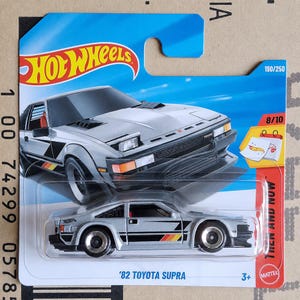 May include: A silver '82 Toyota Supra Hot Wheels die-cast toy car in its original blue and white blister packaging. The packaging features the Hot Wheels logo, the text 190/250, 8/10, Then and Now, and 3+, with a graphic of the car.