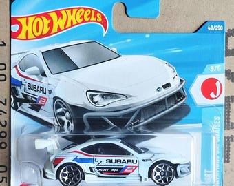 May include: A white Hot Wheels Subaru BRZ die-cast toy car with blue and red accents. The car features the Subaru logo and the number 2. The packaging includes the Hot Wheels logo and the text "SUBARU BRZ".