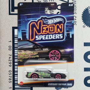 May include: A Hot Wheels Neon Speeders die-cast car in black and pink. The car has a dragon graphic and pink wheels. The packaging displays "Neon Speeders" and "Nissan Silvia (S13)".