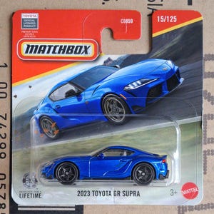 Può includere: Un'auto giocattolo pressofusa 2023 Toyota GR Supra blu nella sua confezione originale Matchbox. La carta presenta una grafica dell'auto su una strada tortuosa, il logo Matchbox, il testo 15/125 e il marchio ufficiale Toyota con licenza.