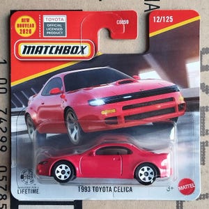 Op de afbeelding: Een rode 1993 Toyota Celica Matchbox-auto op een rood en gele kaart. De verpakking bevat het Matchbox-logo, het Toyota-logo en de tekst "NEW 2020". De auto is een gegoten model.