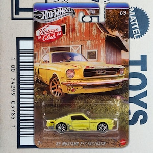 May include: A Hot Wheels Silver Series die-cast model of a yellow '65 Mustang 2+2 Fastback. The packaging features a vintage barn scene and the text "Vintage 19 Club 68". The car is a 1/5 scale model.