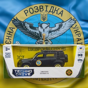 May include: A black Land Rover Defender 110 toy car in a box, with the text "TECHNO DRIVE" and "LAND ROVER DEFENDER 110". The box is set against a Ukrainian flag background.