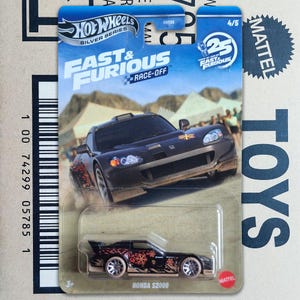 Op de afbeelding: Een Hot Wheels Silver Series Fast & Furious Race-Off Honda S2000 speelgoedauto van gegoten metaal in de originele blauw-witte blisterverpakking. De zwarte auto heeft oranje sneeuwvlokafbeeldingen op de zijkant en zilveren wielen.