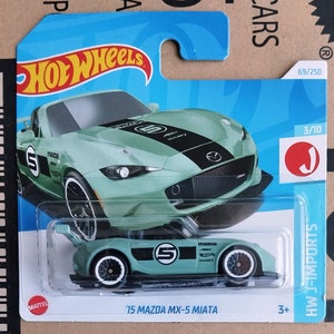 Może przedstawiać: Zielony miętowy model odlewu ciśnieniowego '15 Mazda MX-5 Miata. Samochód ma czarne pasy wyścigowe, numer 5 i koła z białymi obręczami. Opakowanie zawiera logo Hot Wheels i "HW J-IMPORTS".