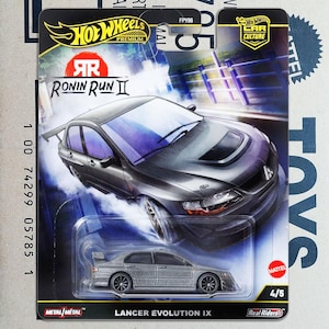 May include: A Hot Wheels Premium die-cast model of a grey Lancer Evolution IX car. The packaging features the "Ronin Run II" logo and "Car Culture" branding. The car is a 4/5 model with "Real Riders" tyres.