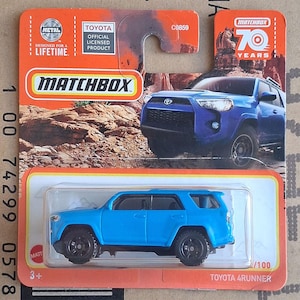 Könnte beinhalten: Ein blaues Matchbox Toyota 4Runner Druckguss-Spielzeugfahrzeug in der originalen orange-weißen Blisterverpackung. Die Verpackung zeigt eine Grafik eines blauen Toyota 4Runner, das Matchbox 70 Years Logo und offizielles Toyota-Branding.