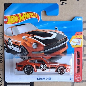 May include: An orange and black Hot Wheels Datsun 240Z die-cast car. The toy car has the number 23 on the side and is packaged in a blue and orange Hot Wheels card. The package reads "Then and Now".
