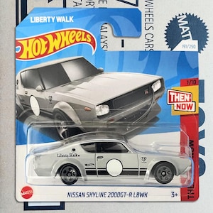 Può includere: Un'auto giocattolo Hot Wheels Nissan Skyline 2000GT-R LBWK color argento nella sua confezione blister originale blu e bianca. L'auto presenta strisce laterali nere, un cerchio bianco sulla portiera e il marchio Liberty Walk. La carta riporta il testo Then and Now.