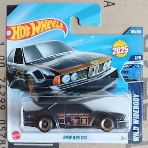 Puede incluir: Un modelo a escala Hot Wheels de un BMW 635 CSi negro y dorado. El coche presenta ruedas y detalles dorados, con el texto "Hwy 35" y "2025" en el embalaje. El modelo forma parte de la serie Wild Widebody.