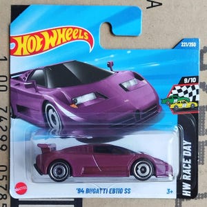 May include: A purple Hot Wheels die-cast toy car of a '94 Bugatti EB110 SS model. The car is displayed on a blue and white card with the Hot Wheels logo. The card also features the text "HW Race Day".