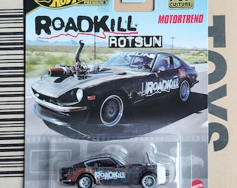 May include: A black 1971 Datsun 240Z die-cast toy car with "Roadkill" and "RotSun" graphics. The car is part of the Hot Wheels Premium line and features Real Riders wheels.