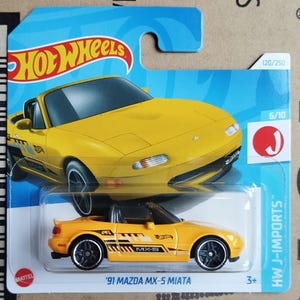 May include: A yellow Hot Wheels 1991 Mazda MX-5 Miata die-cast toy car in its original blue and white blister packaging. The car features black side decals with the text MX-5 and black wheels. The packaging displays the Hot Wheels logo.