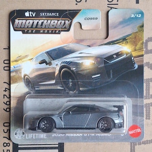 Könnte beinhalten: Ein Matchbox 2020 Nissan GT-R Nismo Modellauto in Grau, verpackt in der originalen Blisterverpackung. Die Karte zeigt den Text Apple TV Skydance Matchbox The Movie, 3/12, C0859 und Mattel sowie eine grafische Darstellung des fahrenden Autos.