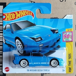 Könnte beinhalten: Blaues Hot Wheels Spielzeugauto eines '96 Nissan 180SX Type X. Das Auto befindet sich auf einer blau-weißen Karte mit dem Hot Wheels-Logo und dem Thema der 90er Jahre. Das Auto hat weiße Räder und ein schwarzes Dach.