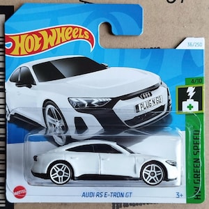 Puede incluir: Un coche de juguete blanco Audi RS e-tron GT de Hot Wheels sobre una tarjeta azul y verde. El coche tiene ruedas negras y el texto "PLUG N GO" en la parte delantera. El embalaje también incluye el texto "HOT WHEELS" y "HW GREEN SPEED".