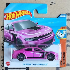 Op de afbeelding: Een roze '20 Dodge Charger Hellcat Hot Wheels modelauto met zwarte details, verpakt in doorzichtig plastic. De verpakking heeft het Hot Wheels-logo, een blauw-oranje achtergrond en de tekst "Muscle Mania".