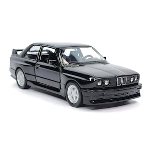 May include: A glossy black model car with silver wheels. The car has a spoiler and detailed headlights. The vehicle is a coupe style with a low profile and a sleek design. The car is set against a white background.