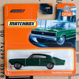 May include: A Matchbox 1966 Dodge Charger die-cast toy car in metallic green, packaged on an orange card. The packaging features the Dodge logo, the text Matchbox, C0859, and a graphic of the car. The toy car is visible through a clear plastic blister.