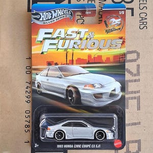 Może przedstawiać: Model samochodu Hot Wheels Silver Series 1/5 Fast & Furious, 1993 Honda Civic Coupe EX EJ1 w kolorze srebrnym. Opakowanie zawiera tło z zachodem słońca, logo Fast & Furious oraz emblemat z okazji 25-lecia serii.