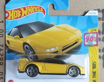 May include: A yellow '90 Acura NSX die-cast toy car on a blue and white card. The car has a black roof and silver wheels. The card features the Hot Wheels logo and a '90s themed graphic. The packaging reads "HW: The '90s".