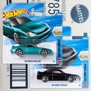 May include: Two Hot Wheels 98 Honda Prelude die-cast toy cars in original blister packaging. One car is metallic teal and the other is black. Both feature silver wheels and are labelled as part of the Factory Fresh series, numbered 5/5 and 136/250.