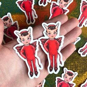 May include: A set of red devil character stickers with white outlines. The stickers feature a cartoon devil with horns, wings, and a tail. The devil is wearing a red suit and has a mischievous expression.