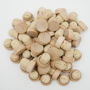 May include: A pile of natural cork bottle stoppers with a wooden top. The stoppers are made of natural cork and have a wooden top that is smooth and unfinished. The stoppers are a light brown colour and are arranged in a pile.