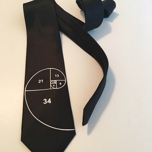 Könnte beinhalten: Eine schwarze Seidenkrawatte mit einer weißen Grafik der Fibonacci-Folge. Die Zahlen 13, 21, 34, 8 und 5 sind auf der Krawatte sichtbar.