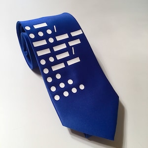 May include: A blue silk tie with a white geometric pattern. The pattern includes circles, rectangles, and lines.
