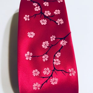 May include: A red silk tie featuring a black and pink cherry blossom design.