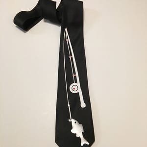 May include: A black silk tie with a white silhouette of a fishing rod and a fish. The fishing rod has a red fishing reel.