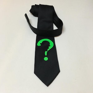 May include: A black silk tie featuring a green question mark design. The question mark is shaped like a person's head wearing a hat.
