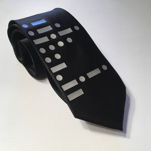 May include: A black silk tie with a white geometric pattern. The pattern is made up of circles and rectangles.