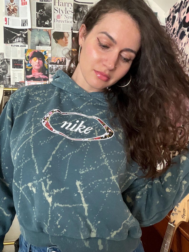 Puede incluir: Sudadera con capucha de color turquesa con dise&ntilde;o de salpicaduras blancas y el logotipo de Nike. El logotipo es un &oacute;valo blanco con el texto Nike y un estampado floral. La sudadera tiene capucha con cord&oacute;n y pu&ntilde;os acanalados.