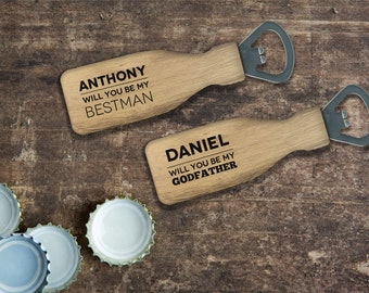 Pode incluir: Dois abridores de garrafas de madeira com topos de abridor de garrafas de metal. O abridor superior diz "ANTHONY WILL YOU BE MY BESTMAN" e o abridor inferior diz "DANIEL WILL YOU BE MY GODFATHER".