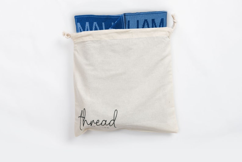 May include: A white cotton drawstring bag with the word "thread" printed on the front. The bag is filled with two blue fabric squares with the word "MALJAM" printed on them.